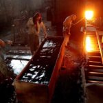 A worker whose shift ended bathes as another worker pulls a heated steel bar from the furnace at a steel mill in Islamabad